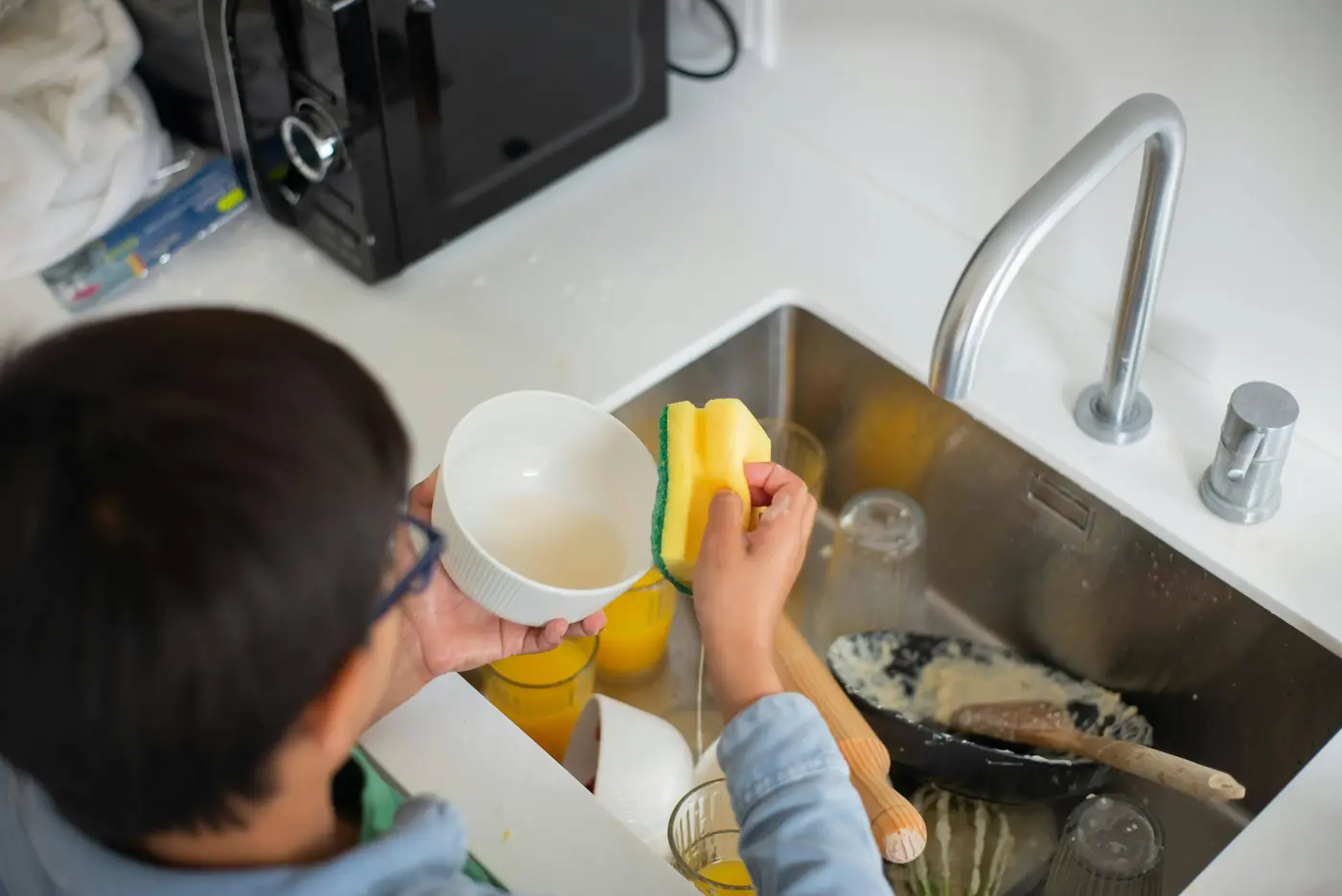 Child learning to wash dishes at the sink